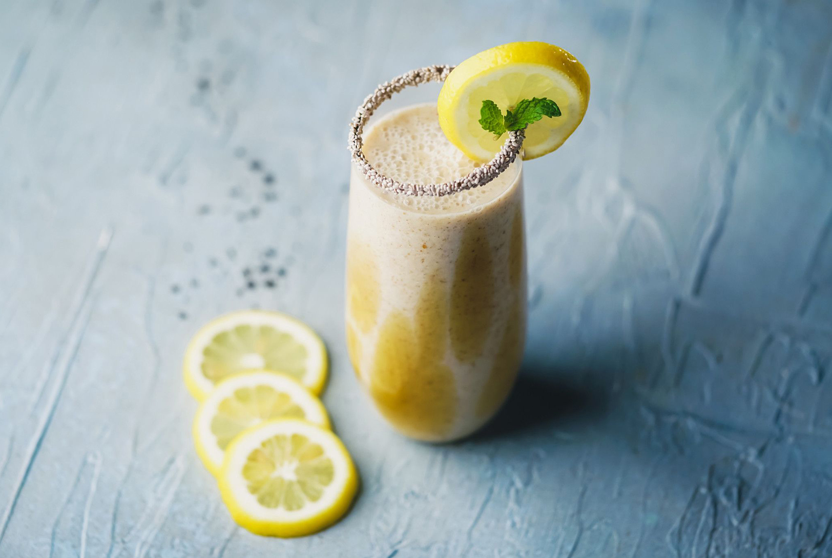 yellow and white smoothie in a tall glass garnished with fresh lemon and mint 