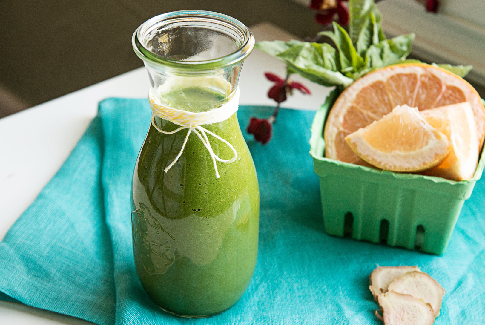 Grapefruit, basil, and ginger smoothie in a tall glass with ingredients displayed.
