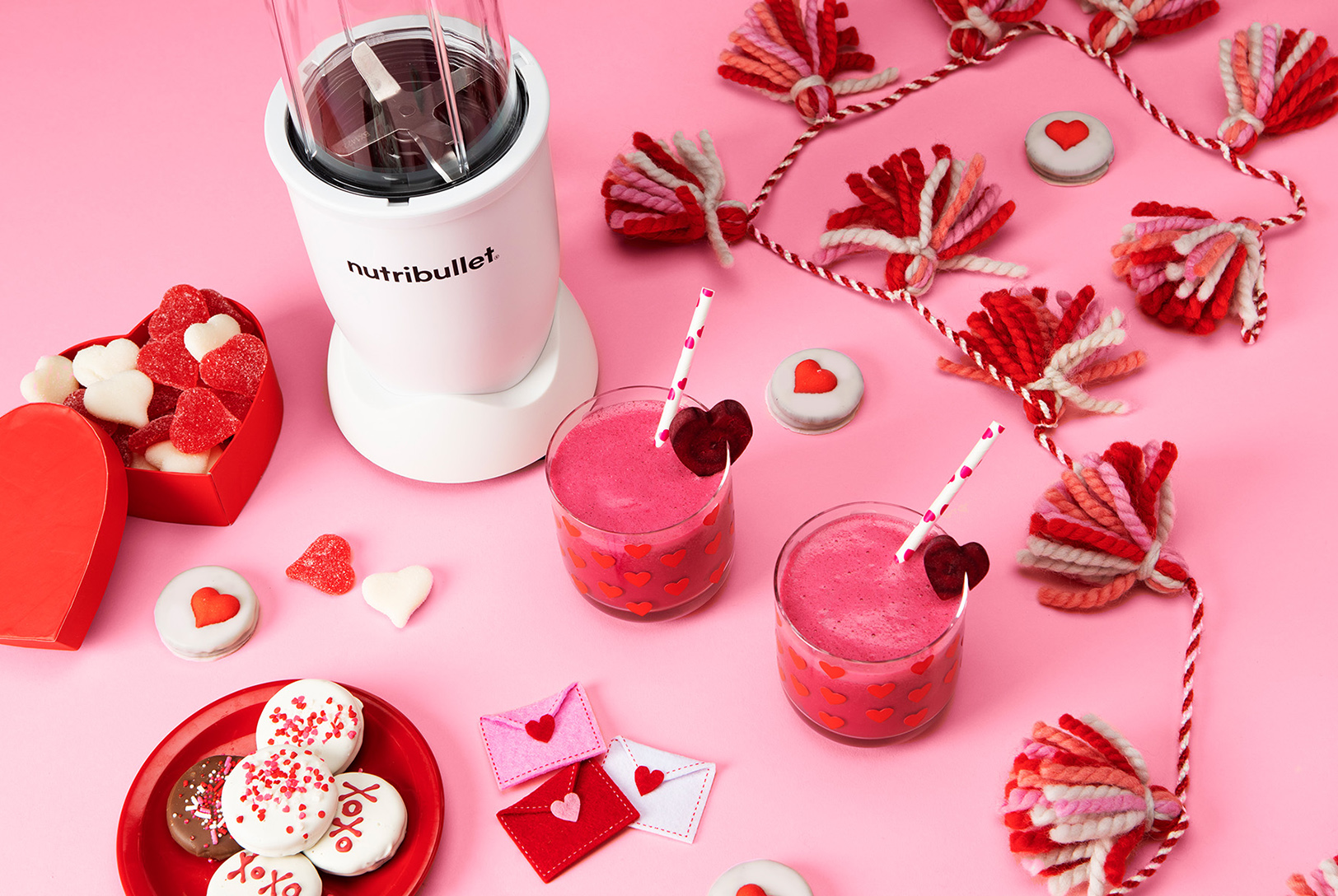 Two glasses of pink smoothies next to a white nutribullet blender with valentine's decor