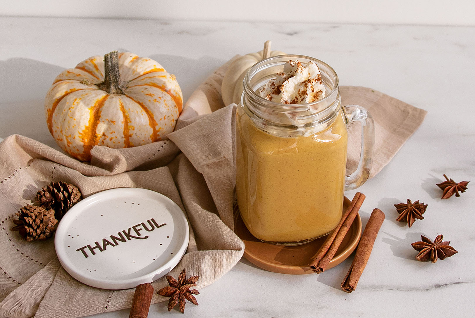 A vibrant pumpkin spice protein smoothie in a glass mug with whipped cream and spice, surrounded by fall decorations.