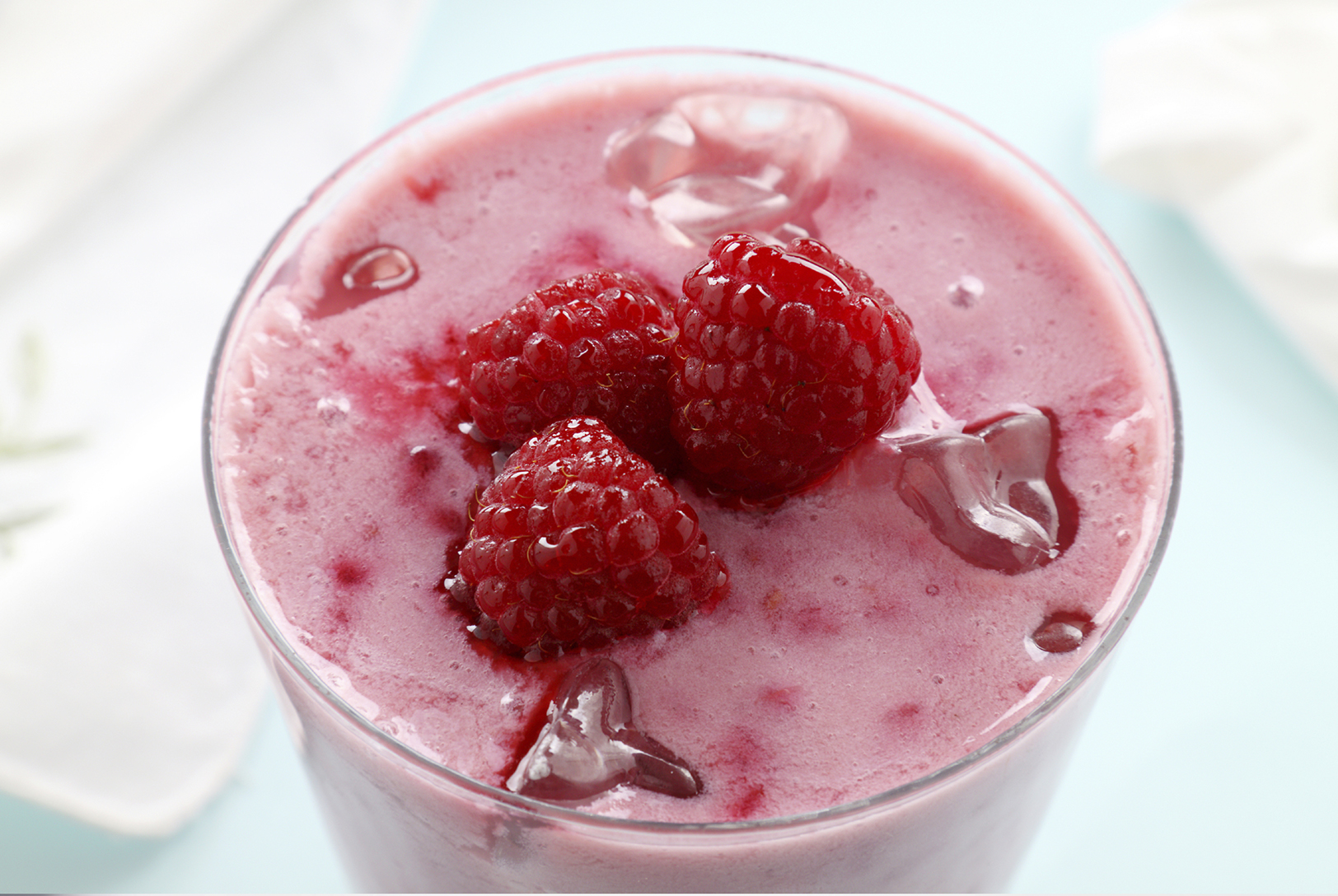 Close-up of a Raspberry Almond Smoothie in a glass, topped with ice cubes and three vibrant red raspberries, viewed from above.