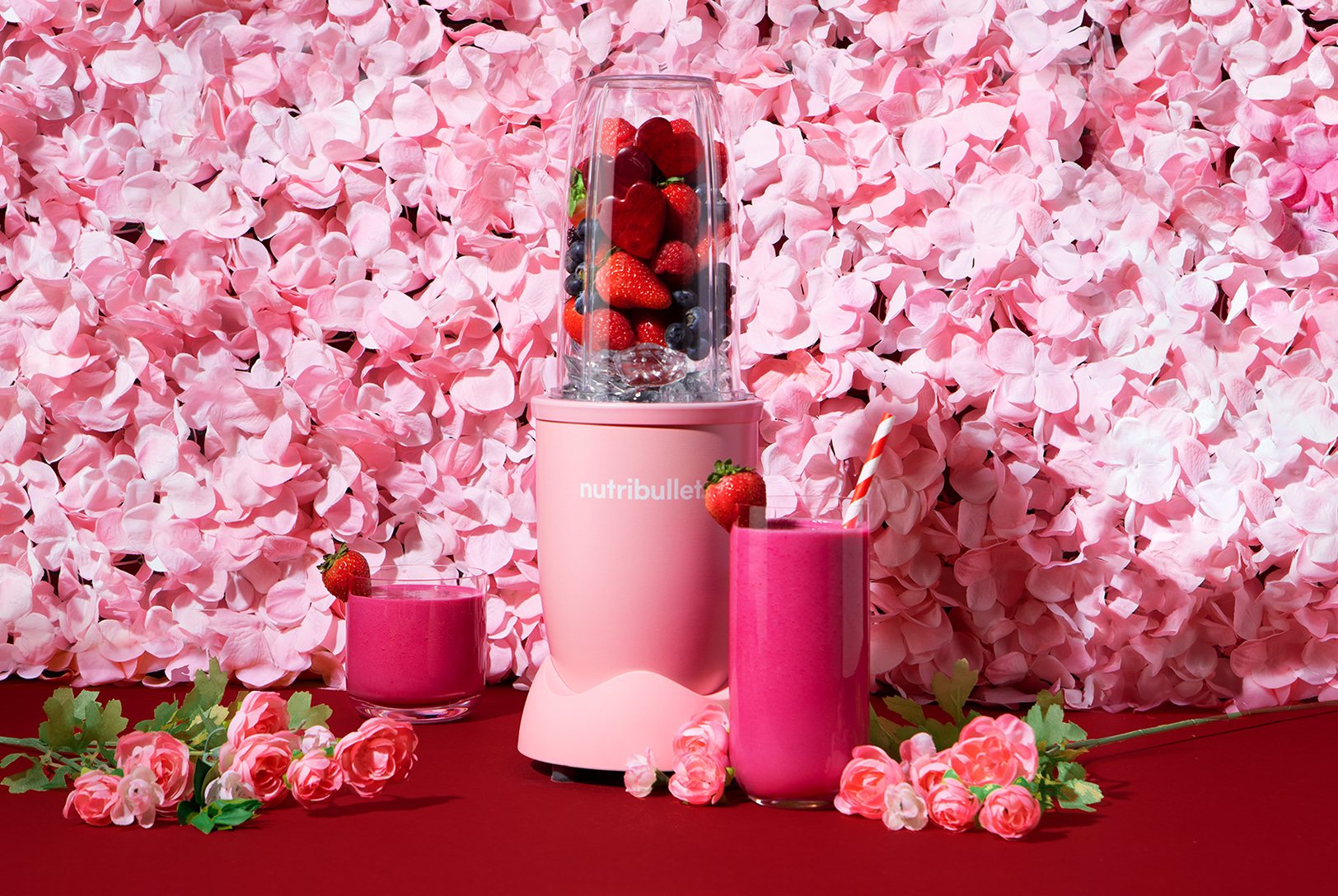 Two glasses of beet smoothie and pink nutribullet blender in front of a floral backdrop 