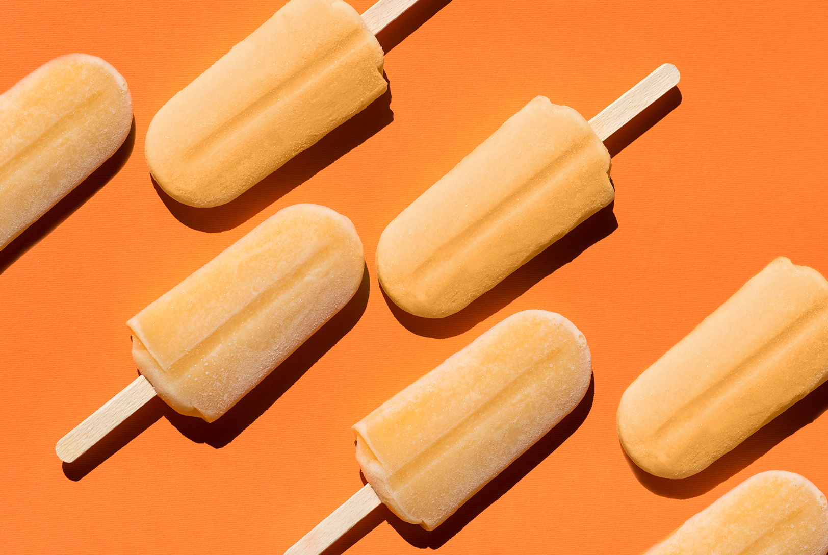 Several orange Citrus Cayenne Ice Pops with wooden sticks arranged on a bright orange background.