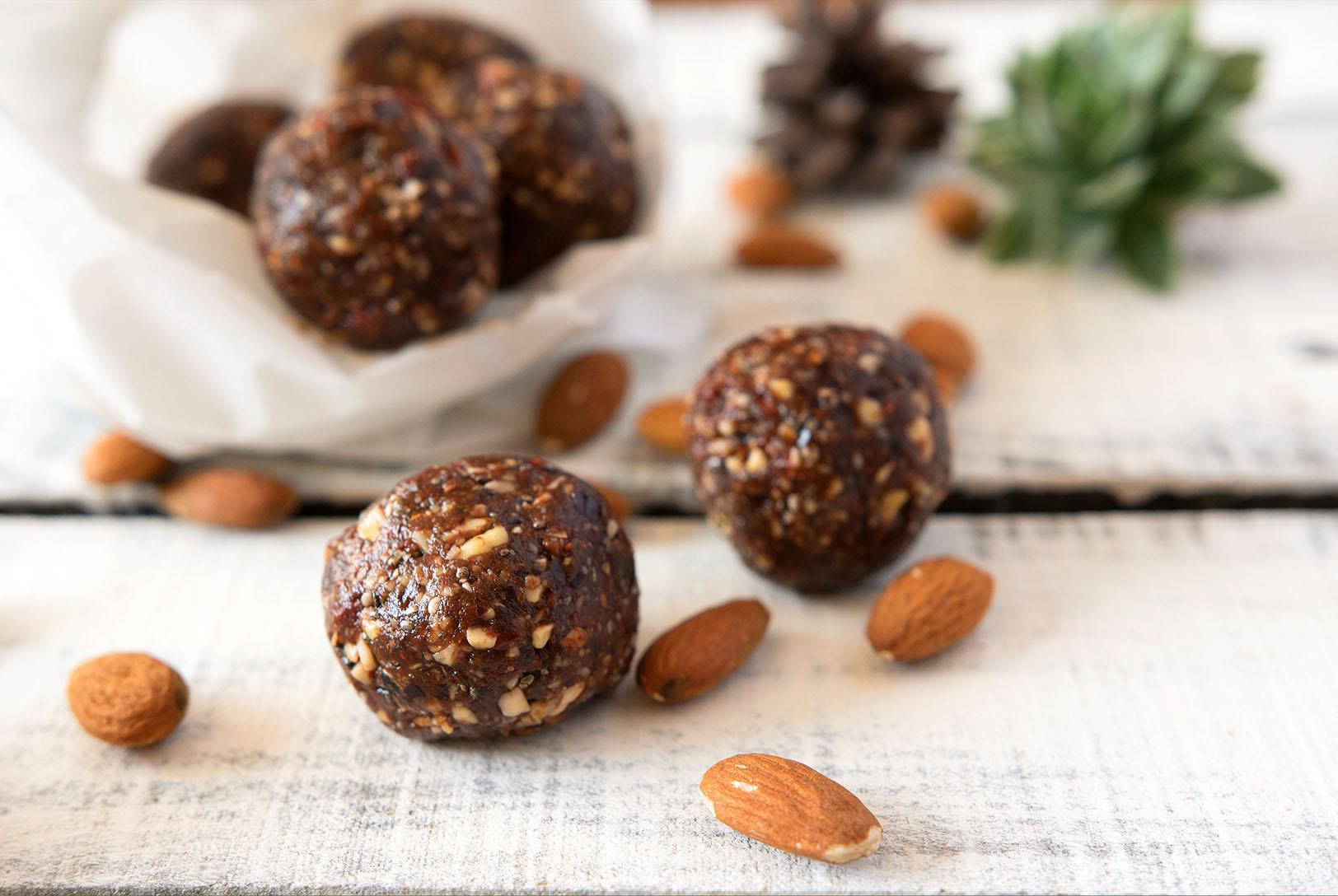 Double Chocolate Energy Bites, some in a white paper liner, surrounded by almonds on a white wooden surface.