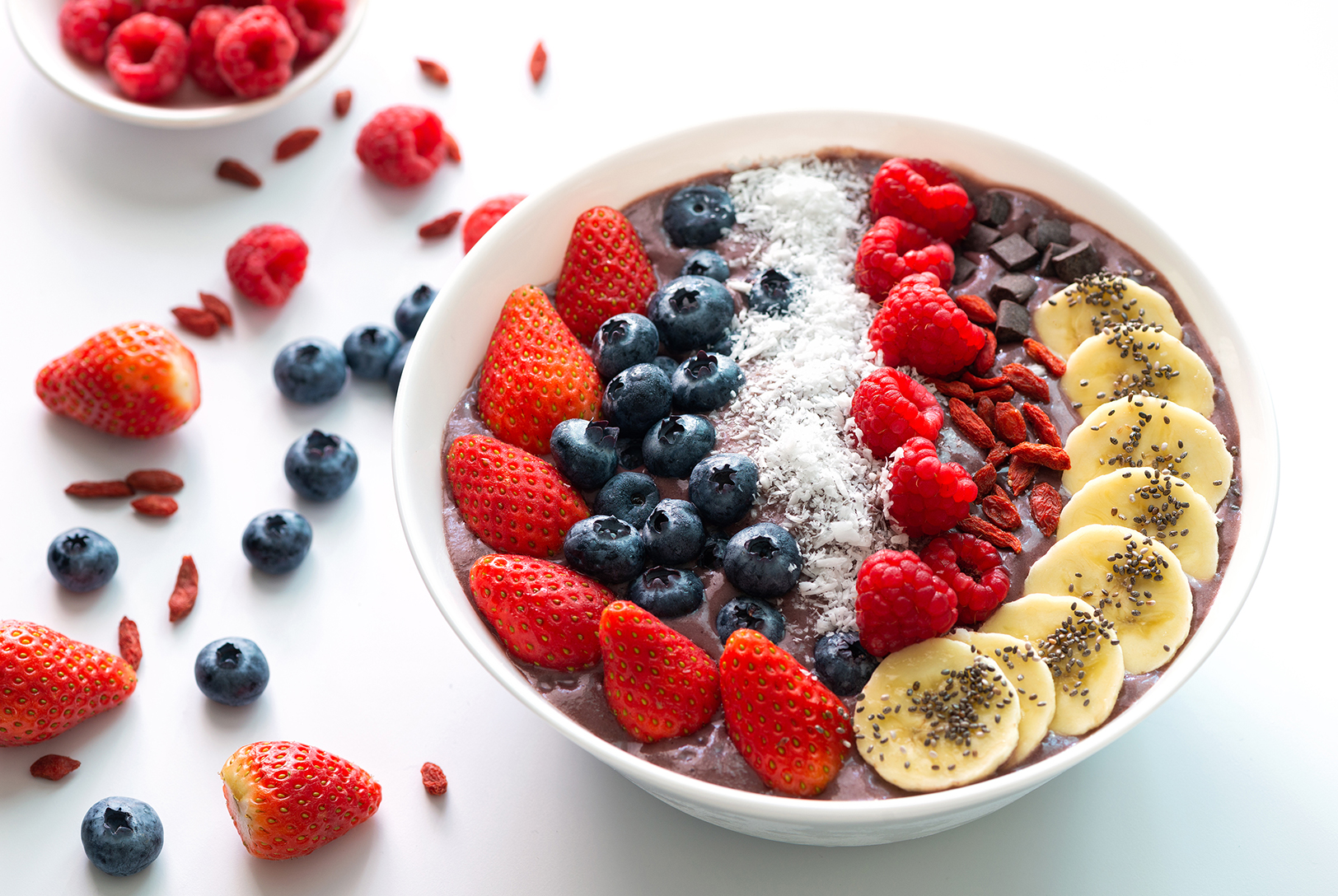 Triple Berry Beet Smoothie Bowl topped with strawberries, blueberries, raspberries, banana slices, coconut flakes, chia seeds, and goji berries.