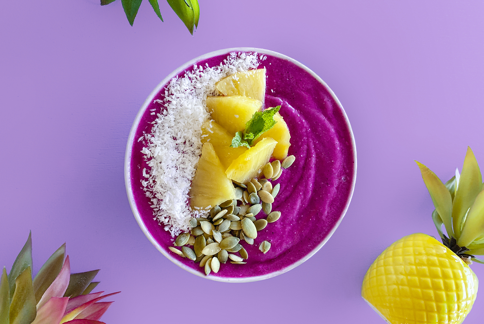 Pitaya and pineapple purple smoothie bowl topped with fresh fruit and seeds.