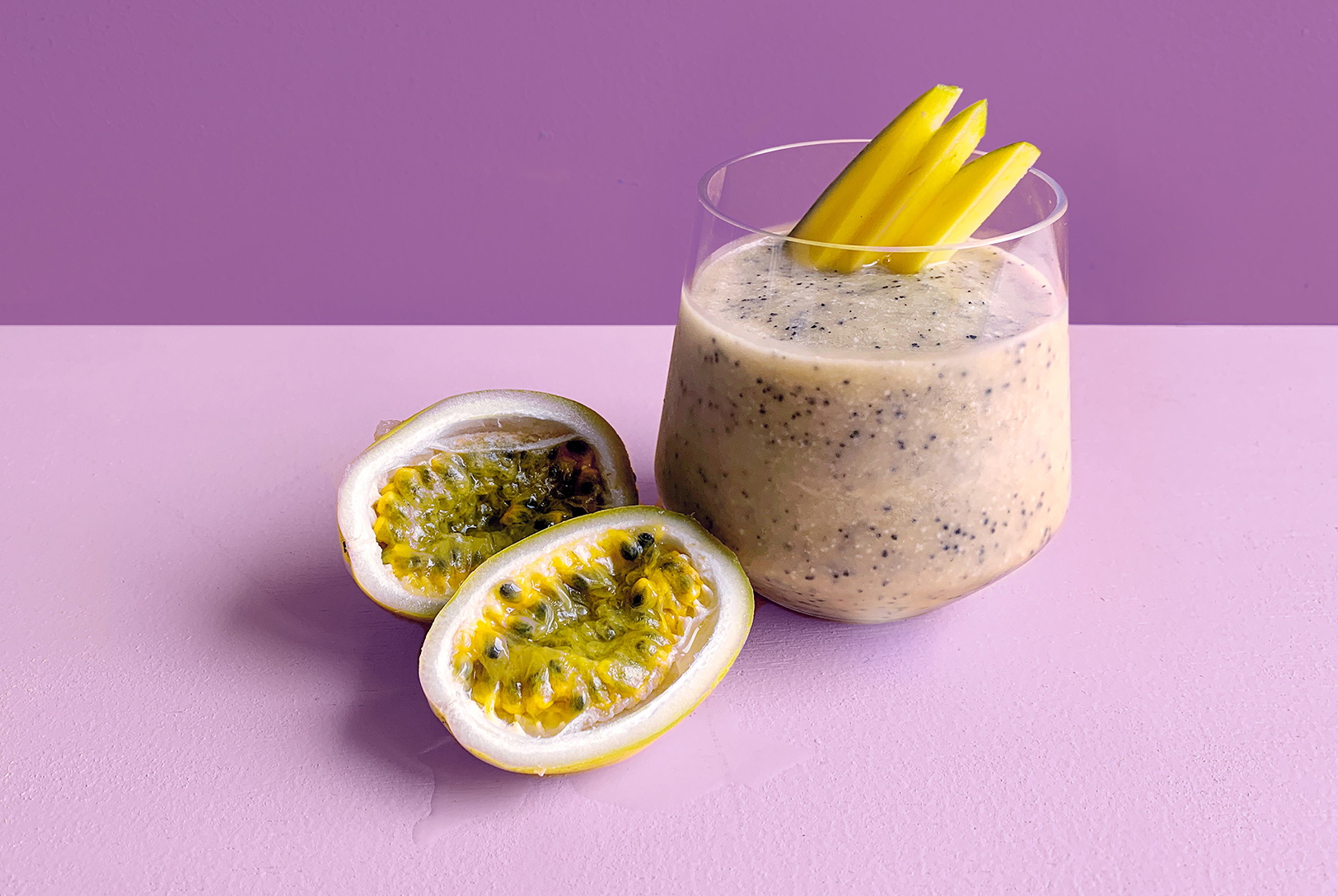 Passion fruit cocktail in a glass with a halved passion fruit garnish with a purple background.