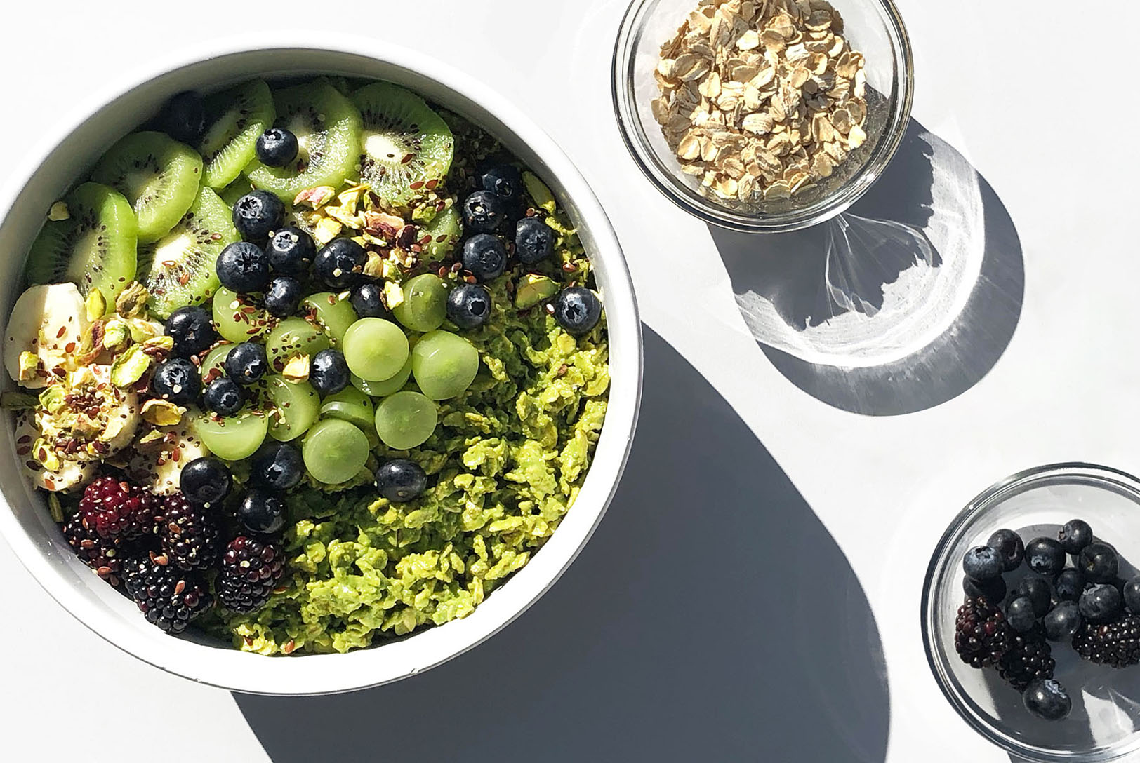 A bowl of green Matcha Pistachio Energy Oats topped with kiwi, blueberries, blackberries, grapes, banana, and pistachios.
