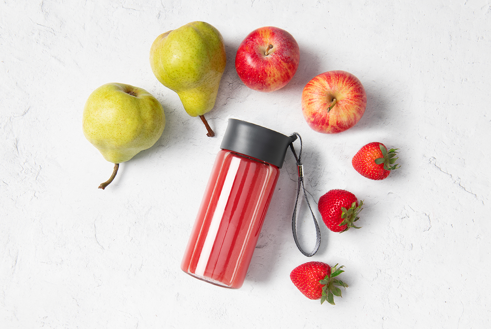 A clear blender cup with a red Apple Pearberry smoothie, surrounded by green pears, red apples, and strawberries on a white surface.