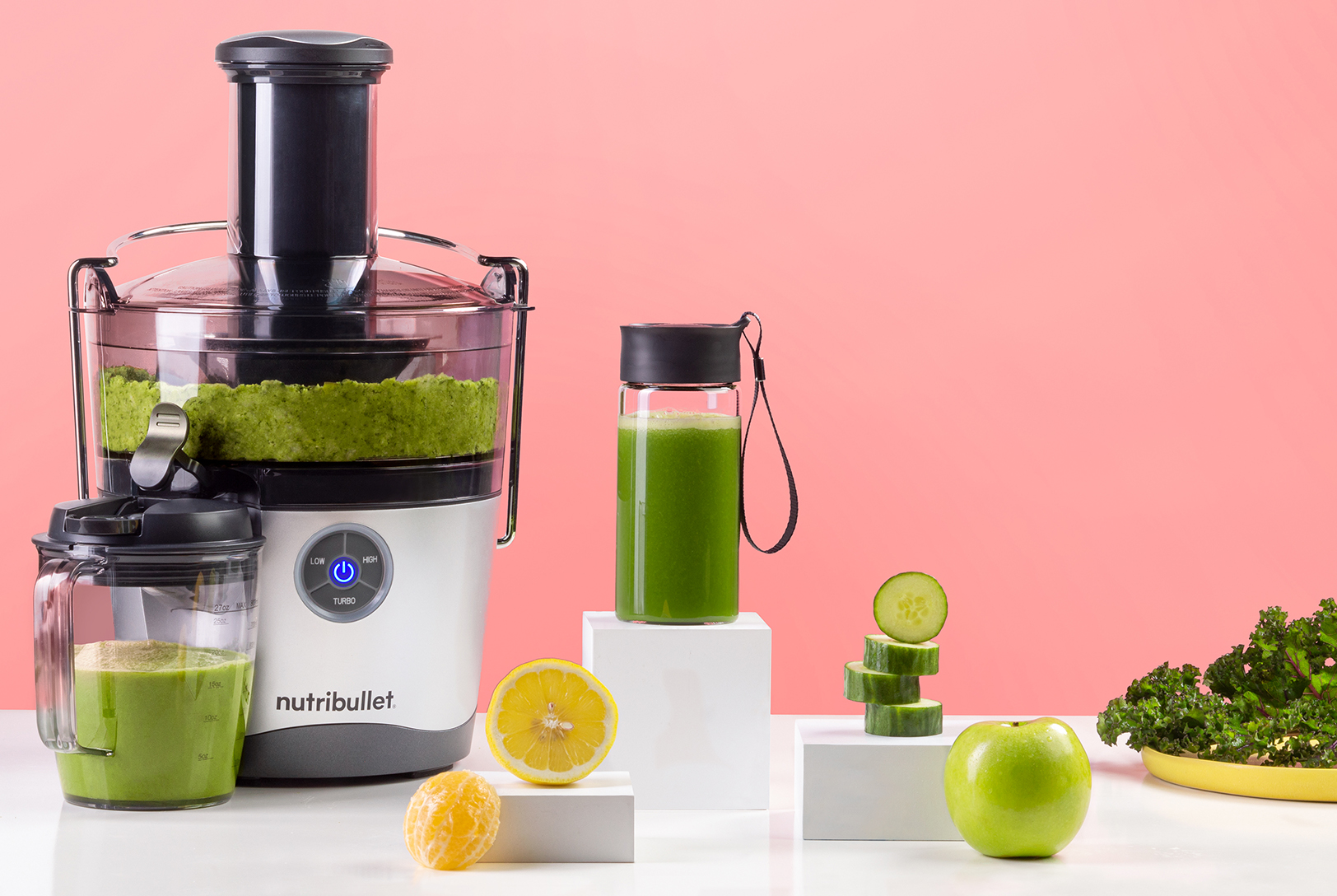 A nutribullet Juicer Pro making green juice, with a bottle of finished green juice, cucumber slices, a green apple, and citrus fruits nearby.