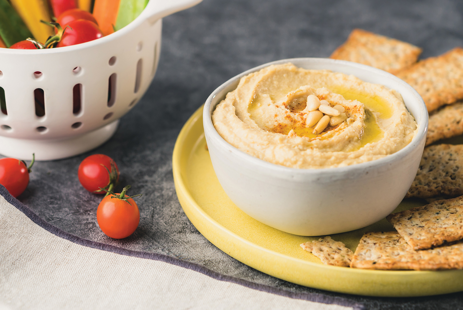 bowl of homemade hummus with pita chips, tomatoes, and fresh vegetables