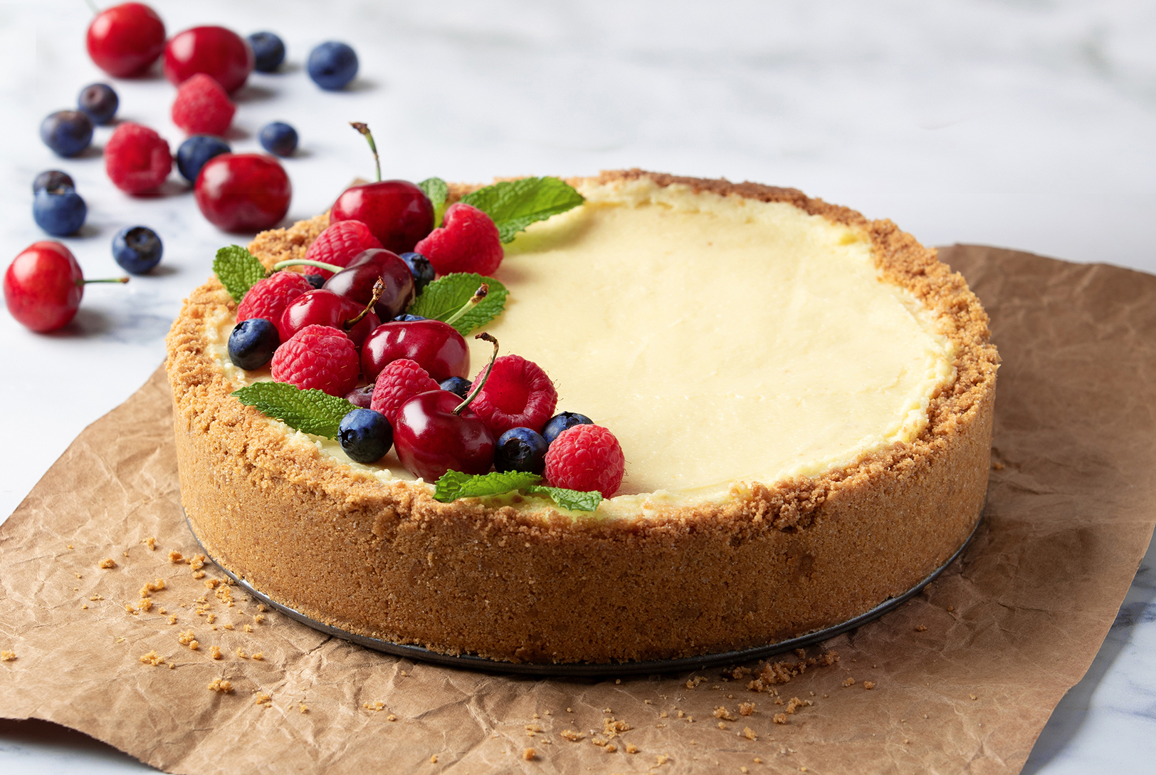 cheesecake with graham cracker crust topped with fresh cherries, blueberries, and raspberries and mint