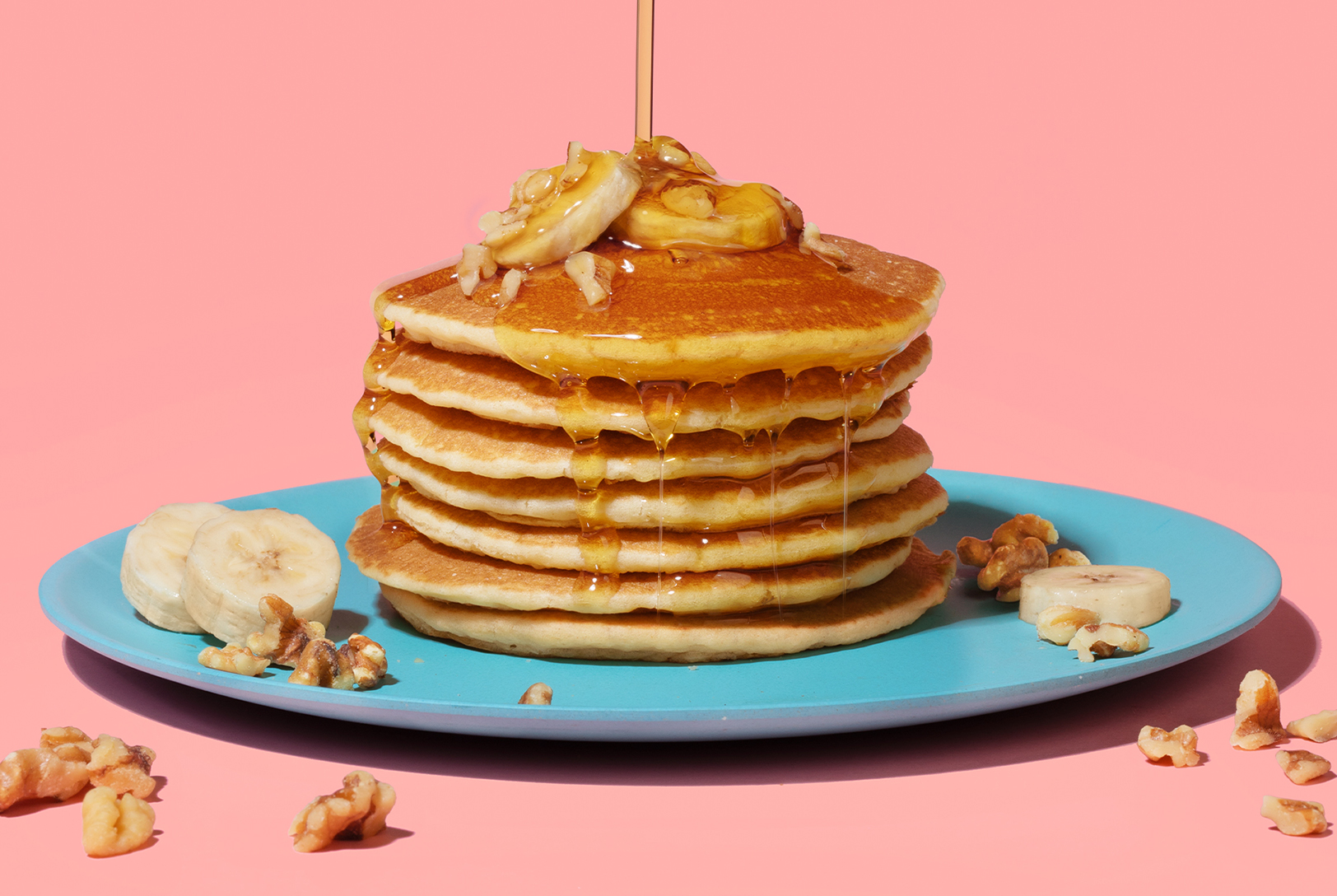 stack of banana pancakes with syrup, banana slices and walnuts
