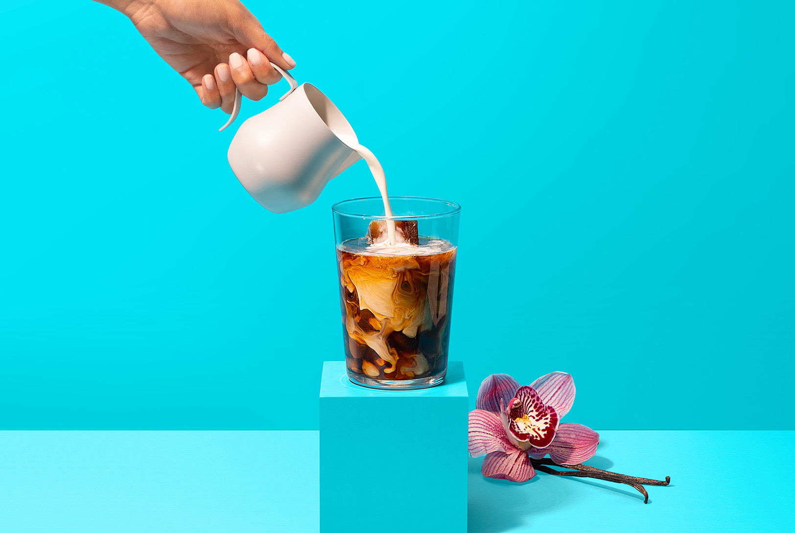 hand pouring almond milk to glass of vanilla iced coffee