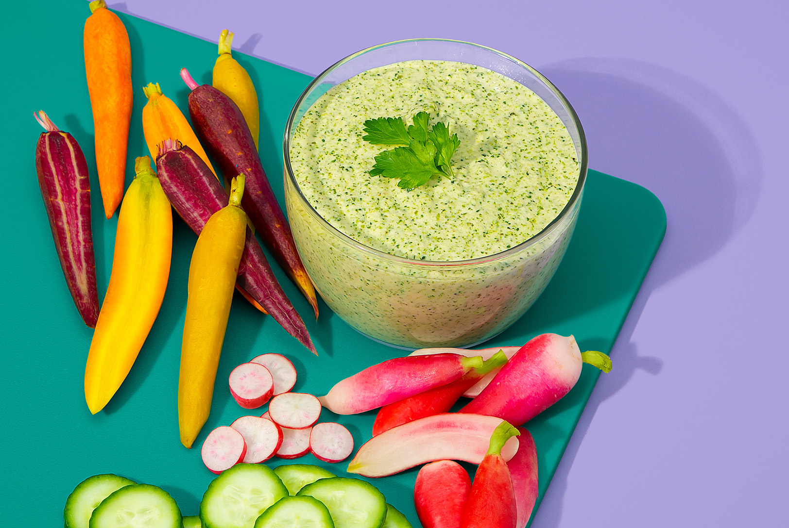 clear bowl of green goddess dressing with fresh carrots and radishes for dipping