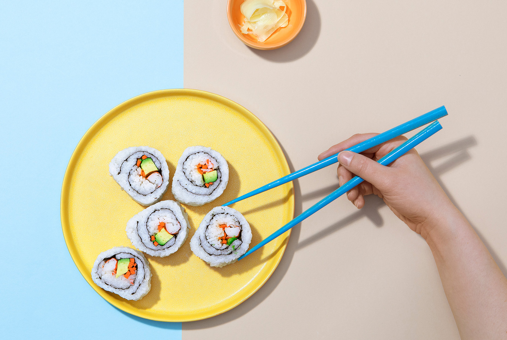 hand picking up California rolls with chopsticks