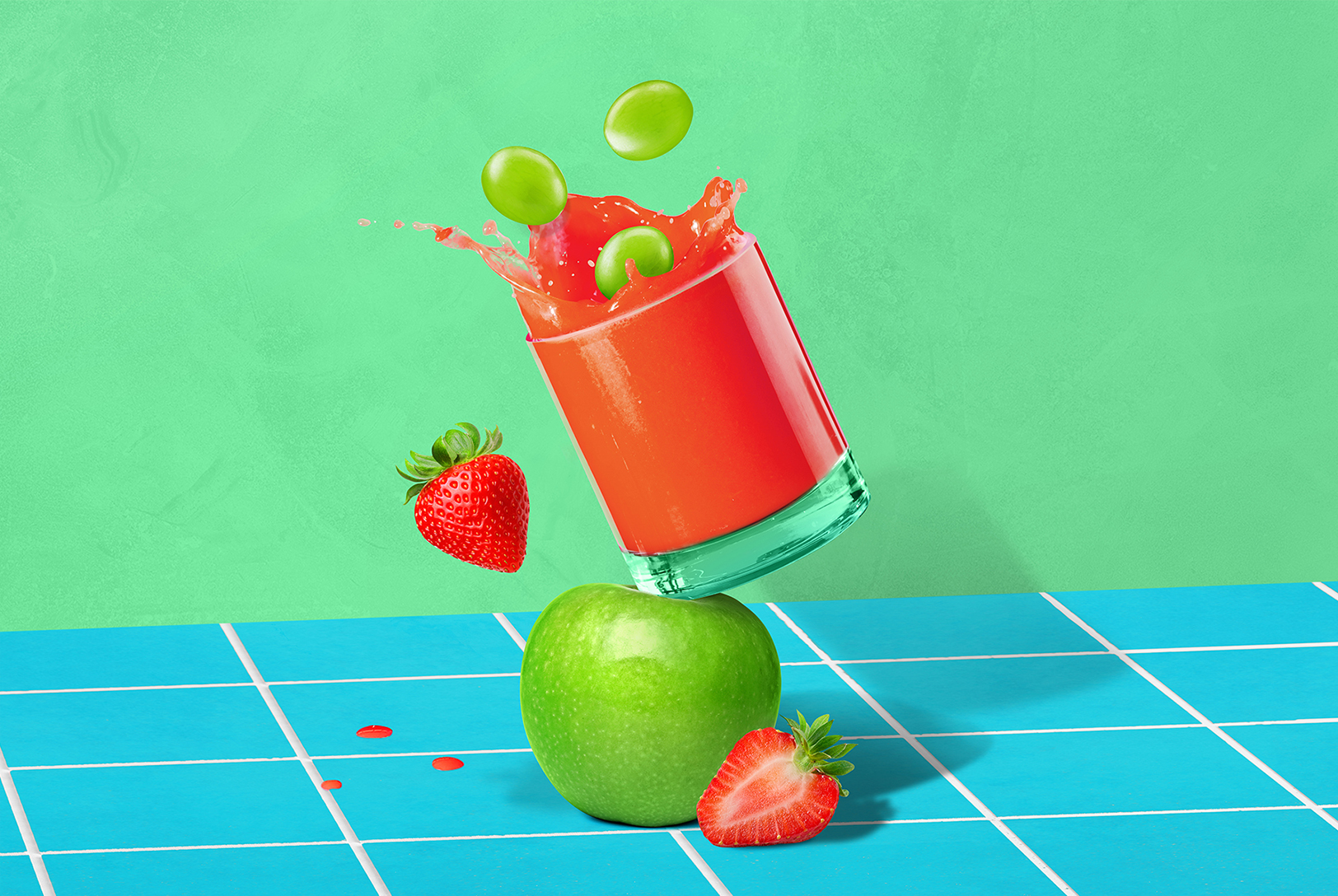 glass of red fruit juice propped on top of a green apple splashing with green grapes, strawberries and green apple on a blue counter with green background