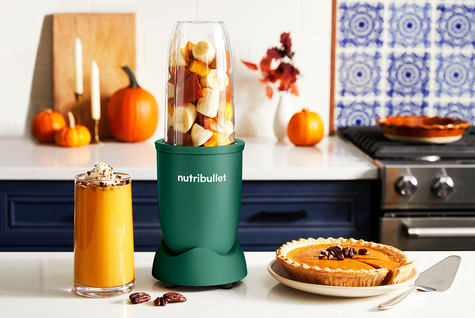 glass of pumpkin pie smoothie next to a green nutribullet blender along with a whole pumpkin pie sitting on kitchen counter