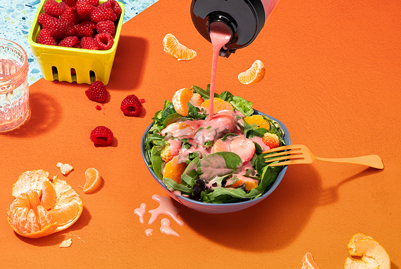 pink raspberry vinaigrette salad dressing poured atop spinach, citrus salad