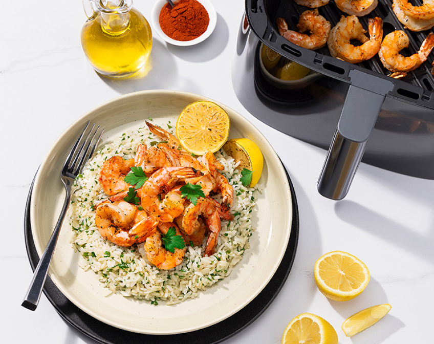 A plate of prawns over herb rice next to cooked prawns inside an open air fryer basket.