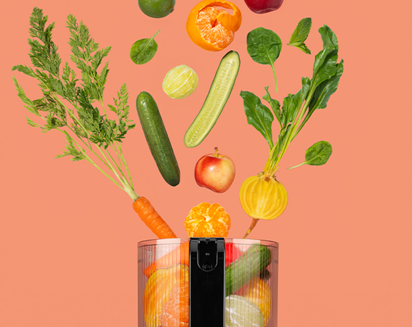 Fresh fruits and vegetables floating into a blender cup on a peach background.