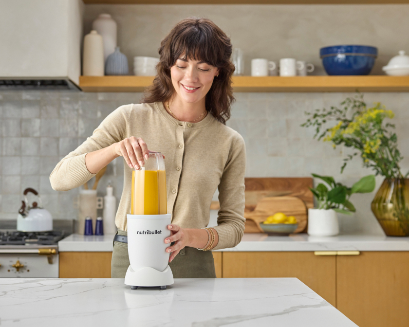 Woman blending a fresh smoothie in a nutribullet blender on a modern kitchen countertop, preparing a healthy drink at home